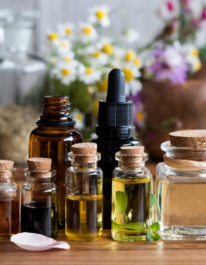 Selection of essential oils with various herbs and flowers in the background