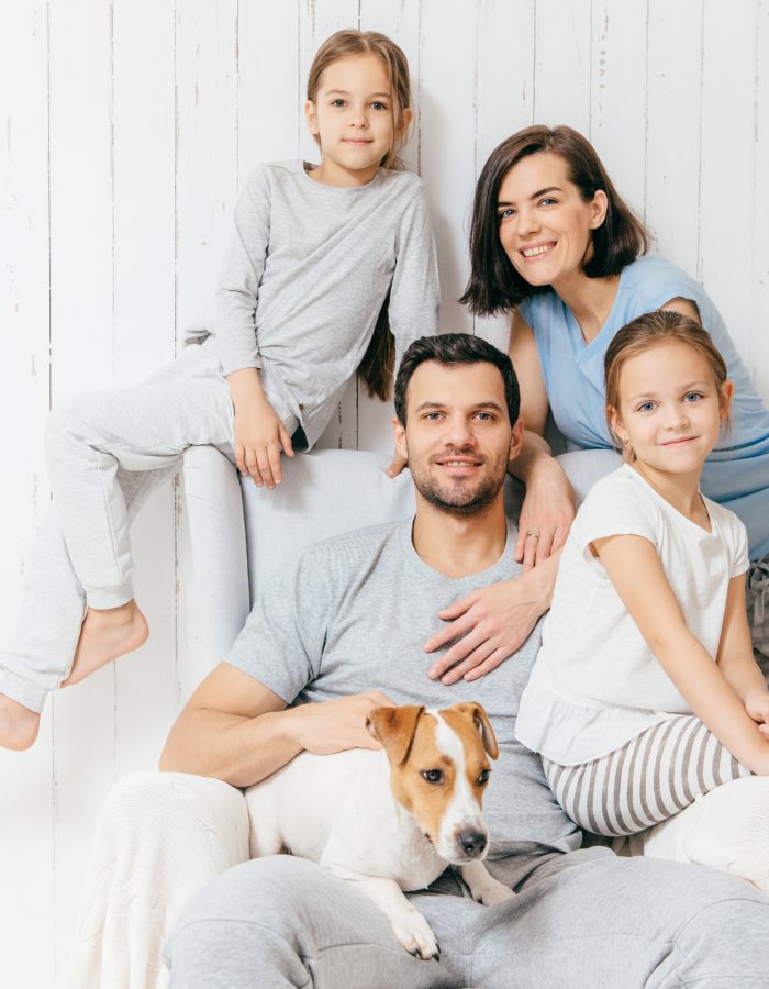 Friendly family of four memebers: cheerful European brunette female, her husband, two daughters and favourite pet, have good relationships, support each other. Affectionate parents with children