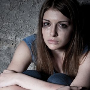 Hopelessness. Top view of young woman crying and looking at camera while sitting against dark wall