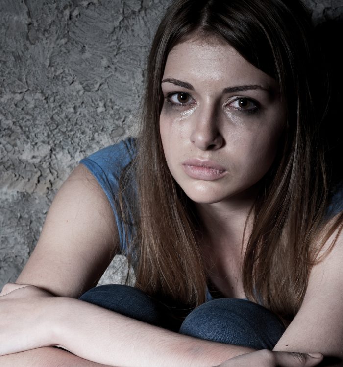 Hopelessness. Top view of young woman crying and looking at camera while sitting against dark wall