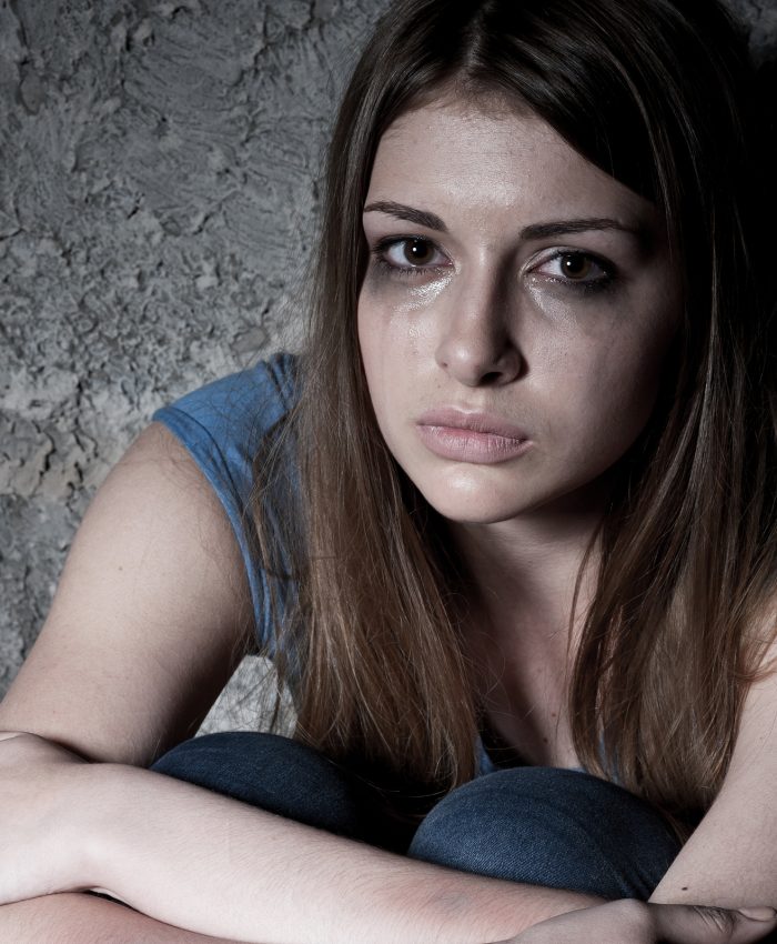 Hopelessness. Top view of young woman crying and looking at camera while sitting against dark wall
