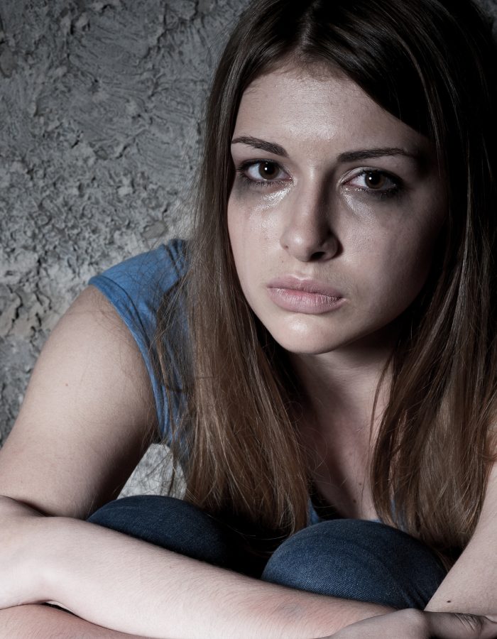 Hopelessness. Top view of young woman crying and looking at camera while sitting against dark wall