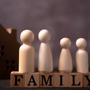 Wooden figures family standing on Wooden cube that writes the word family in front of a wooden house. The concept of Protection and safety, Home Security, property insurance and house.
