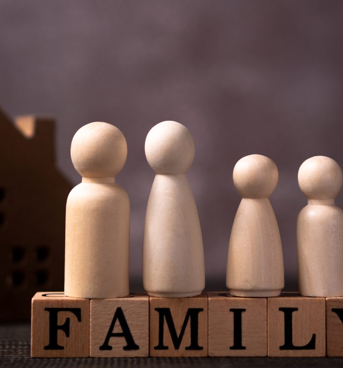 Wooden figures family standing on Wooden cube that writes the word family in front of a wooden house. The concept of Protection and safety, Home Security, property insurance and house.